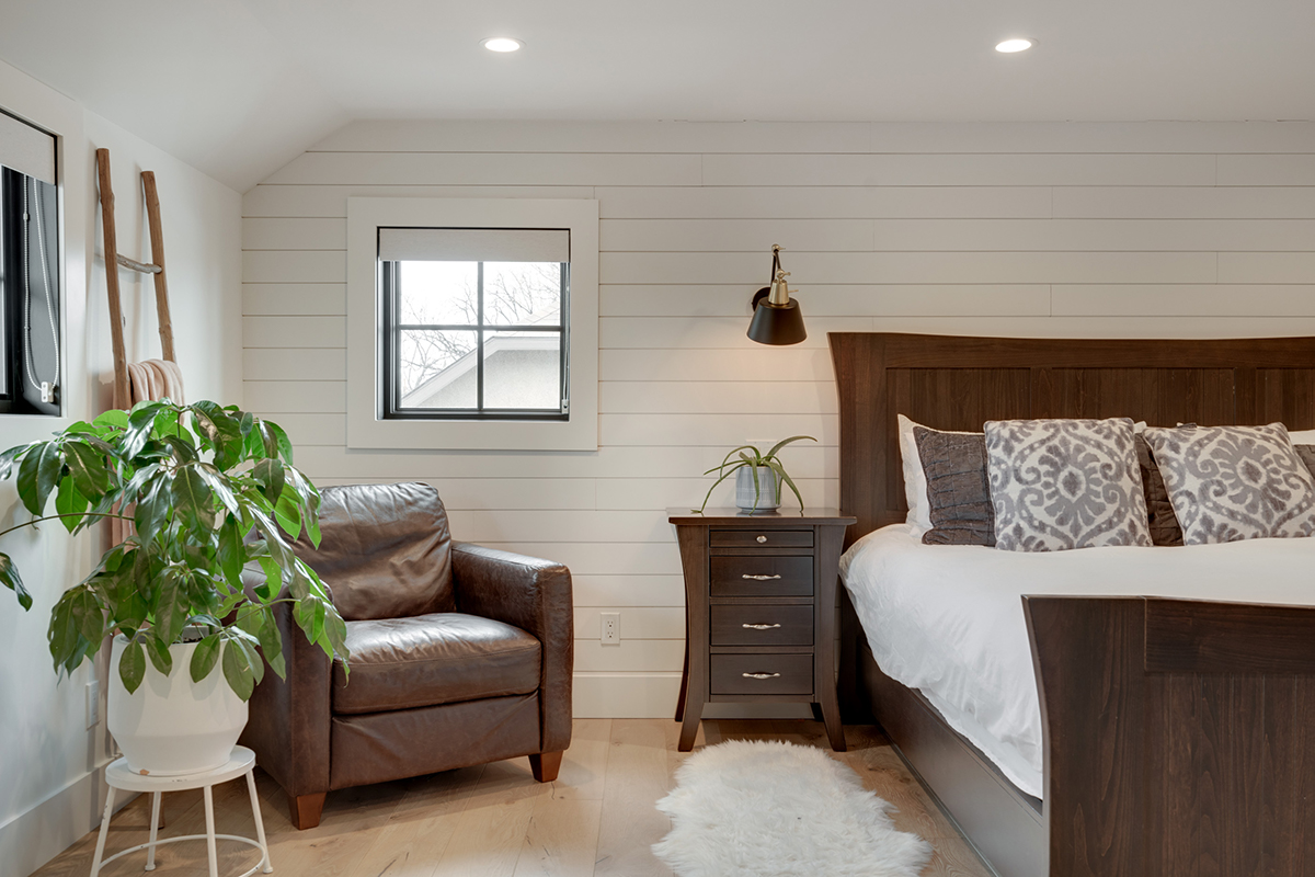 Shiplap wall in bedroom with a plant, chair, and sconce by Creek Stone Fine Homes of Okotoks, AB