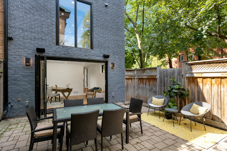 Image of a backyard with dinner table and lounge chairs, with large door that shows beautiful interior of home.