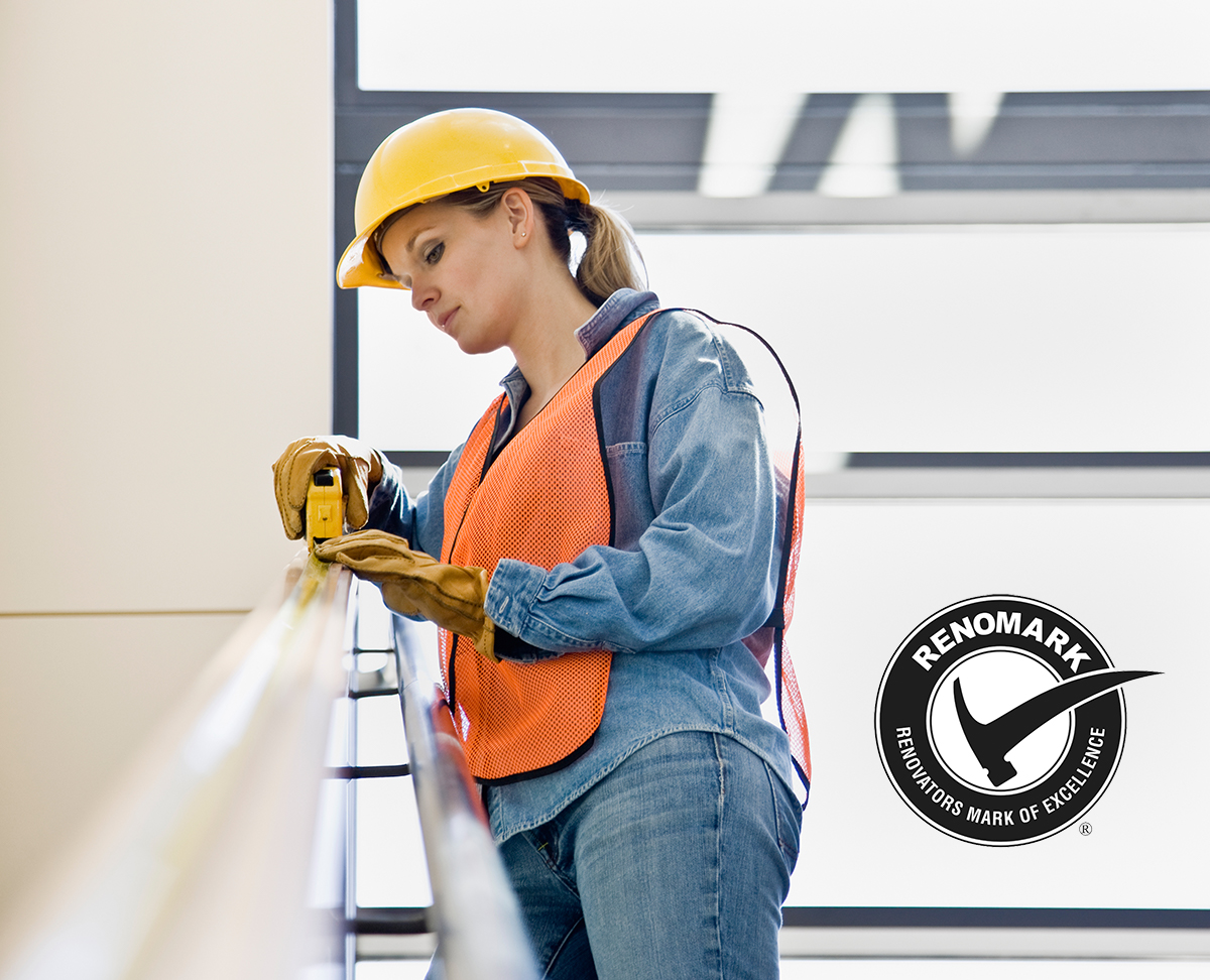 Female contractor wearing hard hat, vest, and glove measuring a railing with RenoMark logo in the bottom right hand corner.