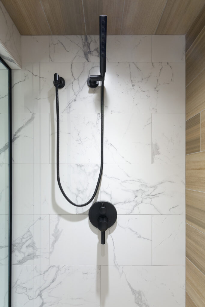 Modern shower with a black handheld showerhead and control set against a white marble-tiled wall. The shower has clean lines and a glass partition is partially visible on the left.