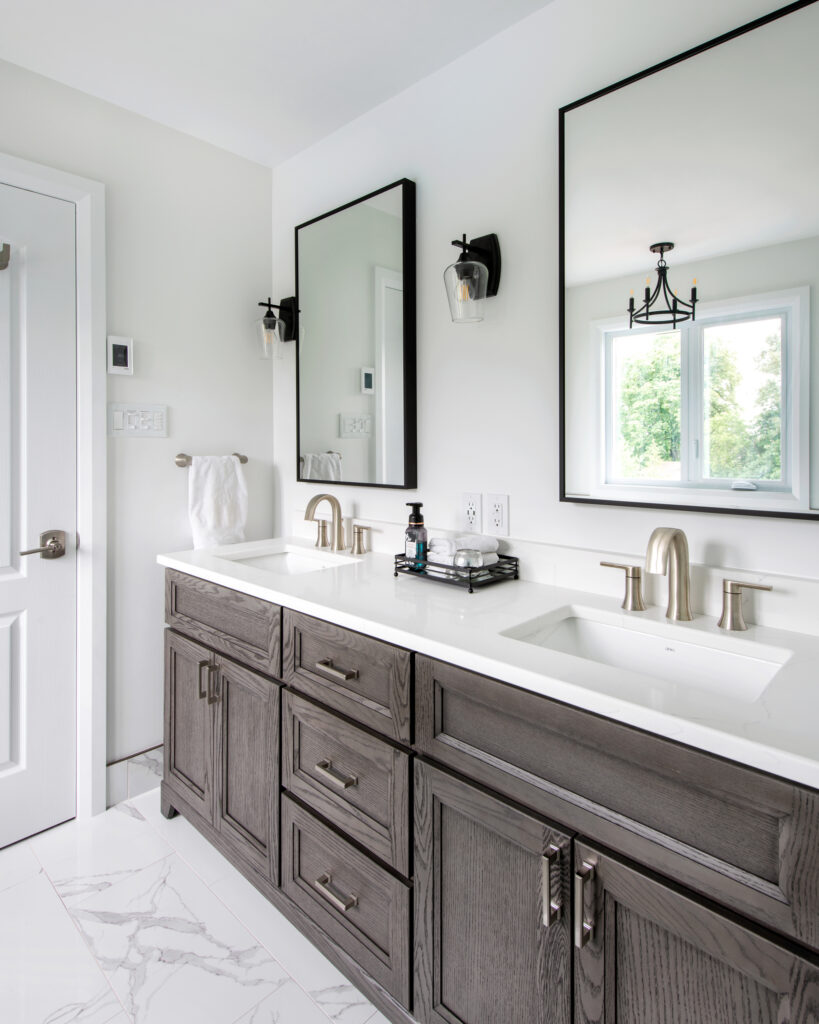 Modern bathroom with double vanity, two rectangular mirrors, brushed nickel faucets, dark wood cabinets, white countertops, marble floor tiles, and a window letting in natural light.