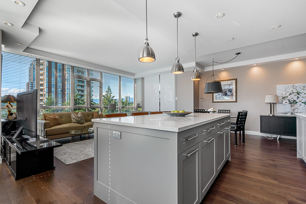 Modern open-concept kitchen and living room with large windows, city views, an island with pendant lights, a dining area, a sofa, TV, and hardwood floors. Natural light fills the stylish, contemporary space.