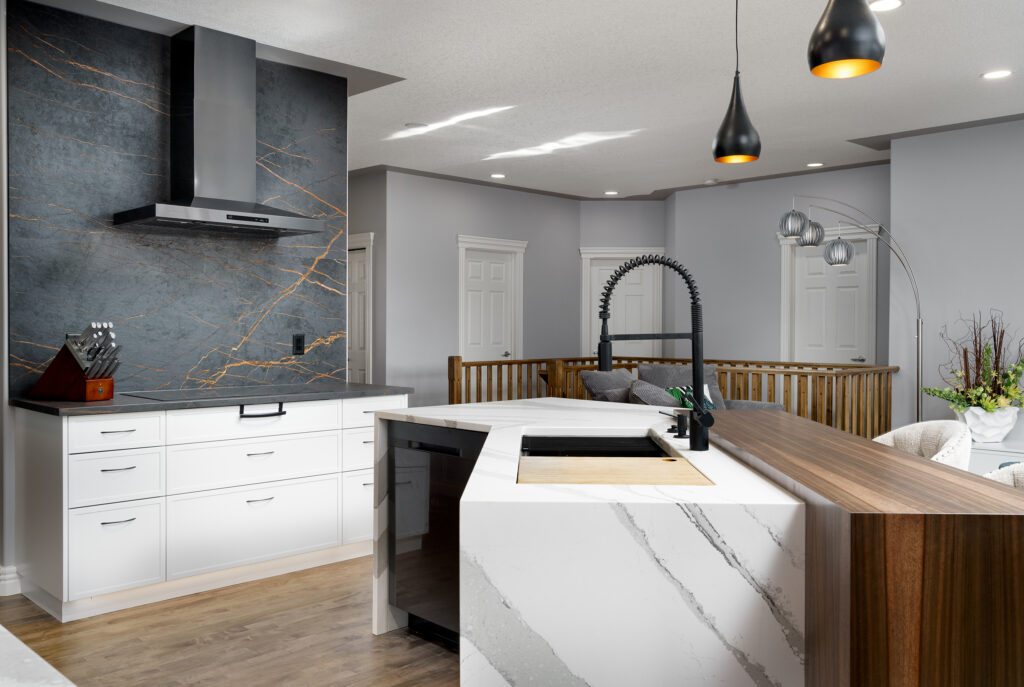 Modern kitchen with white cabinets, a large marble island, black appliances, wood accents, pendant lights, and a unique black faucet. The backsplash features dark stone with gold veining.