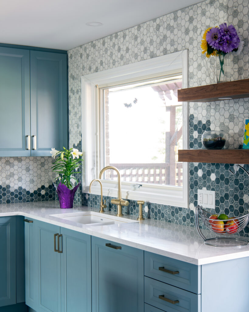 Modern kitchen with blue cabinets, hexagonal tile backsplash, brass fixtures, three globe pendant lights.