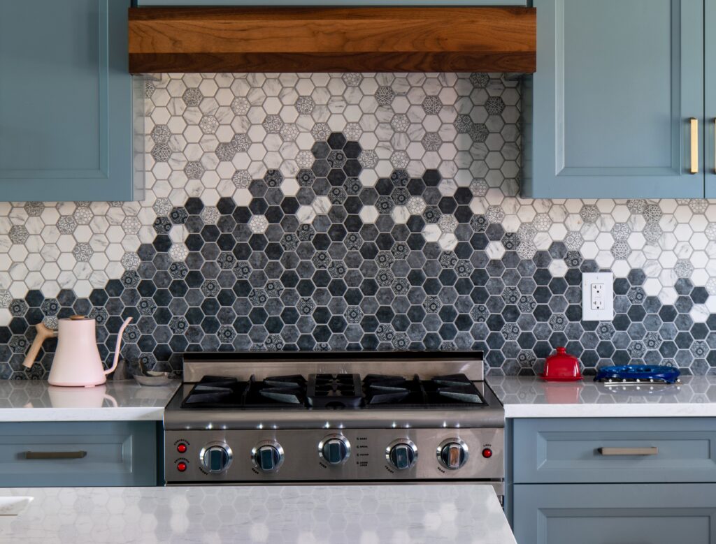 Modern kitchen with blue cabinets, hexagonal tile backsplash, brass fixtures, three globe pendant lights,