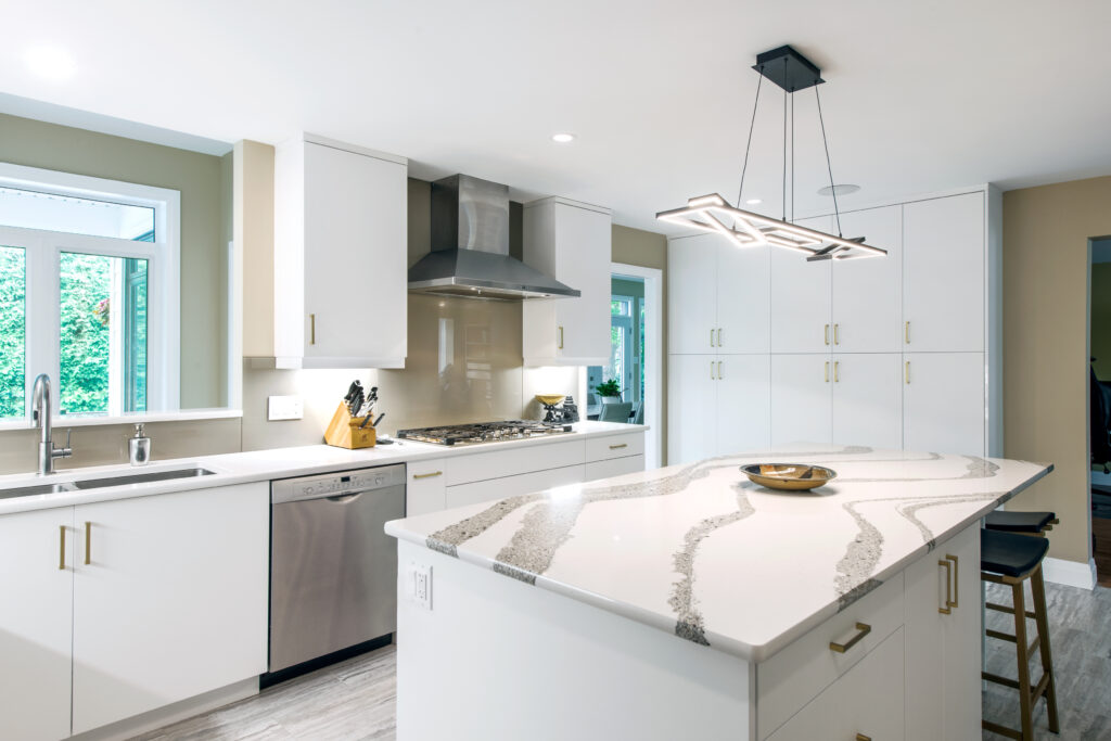 Modern kitchen with white cabinets, stainless steel appliances, a large island with a patterned quartz countertop, a contemporary light fixture, and large windows letting in natural light.