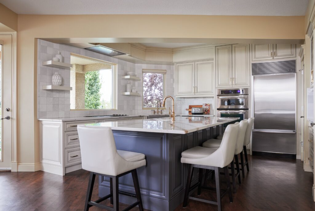 Modern kitchen with white cabinets, stainless steel appliances, a large gray island with a marble countertop, four white cushioned chairs, and wood flooring. Natural light enters through windows.