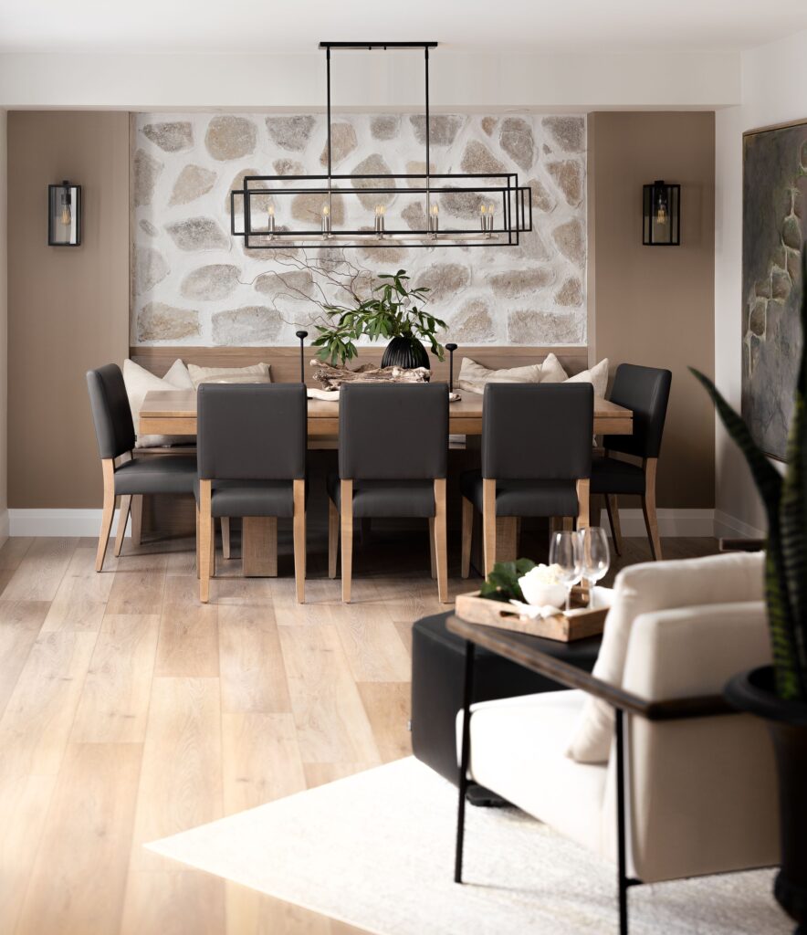 Modern dining room with a wooden table, eight dark chairs, a black metal chandelier, decorative pillows, and a stone accent wall. Light wood flooring and neutral-toned walls create a cozy, contemporary atmosphere.
