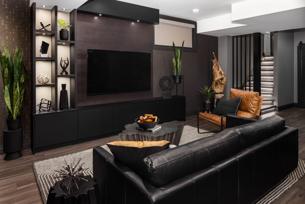 Modern living room with black furniture, leather chairs, a wall-mounted TV, decorative shelving, indoor plants, and geometric decor. Neutral colors and contemporary design create a stylish, comfortable atmosphere.