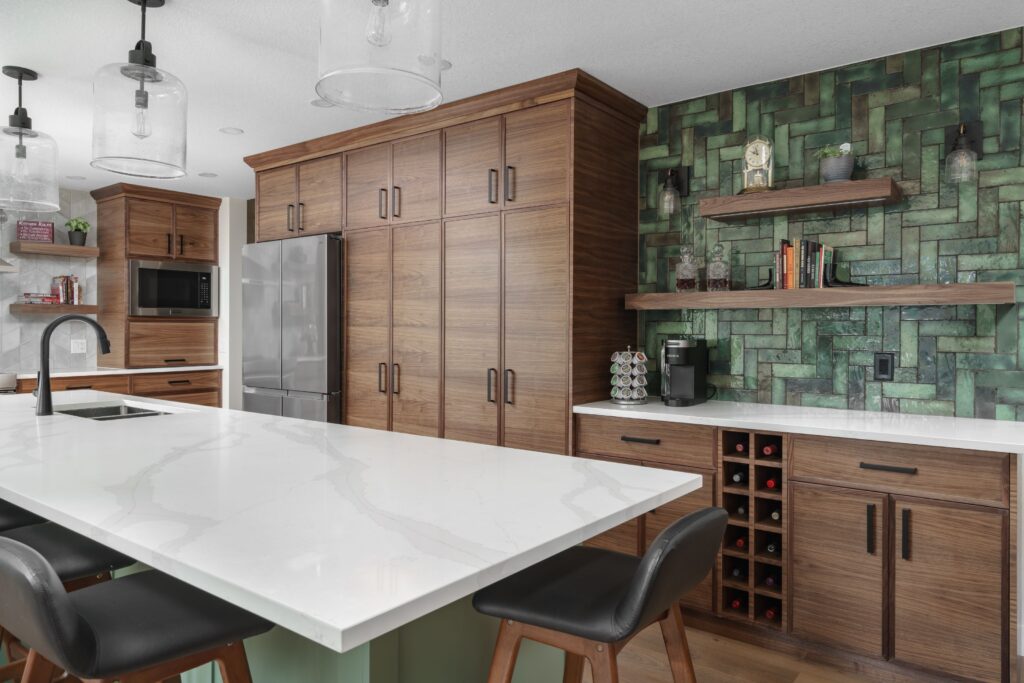 Modern kitchen with dark wood cabinets, a white marble island, black chairs, stainless steel appliances, and a green tiled backsplash with open shelves displaying decor and a coffee maker.