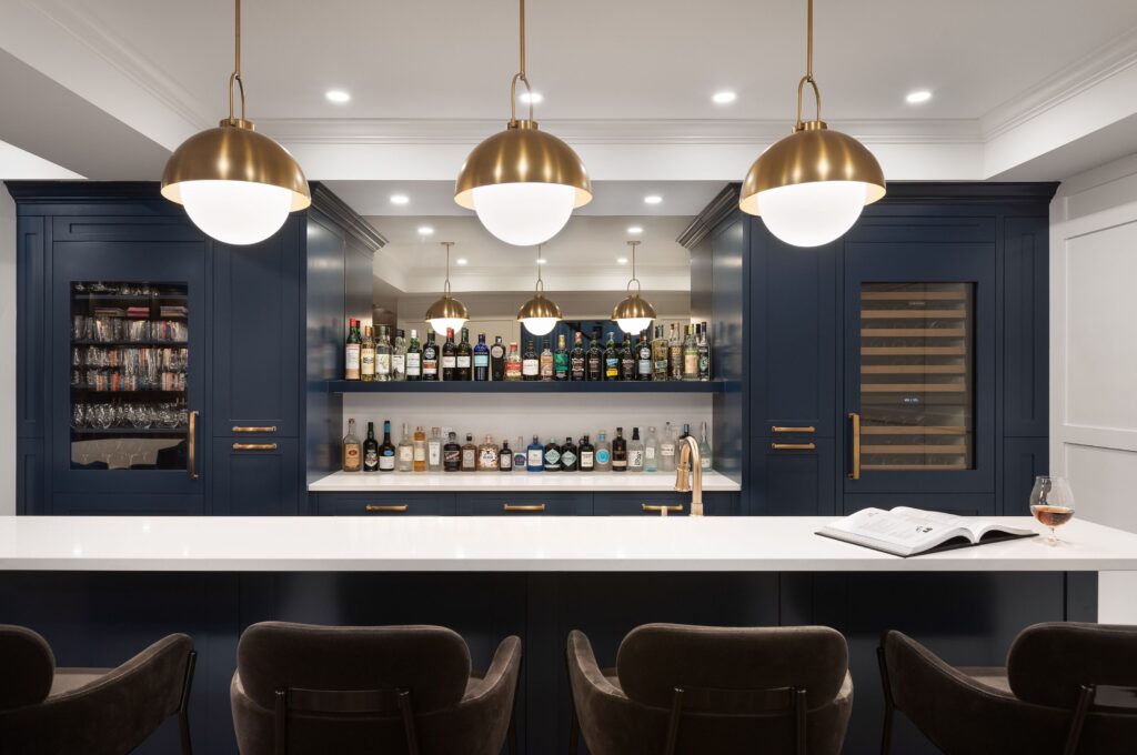 Blue basement bar with gold handles and mirrored backsplash.