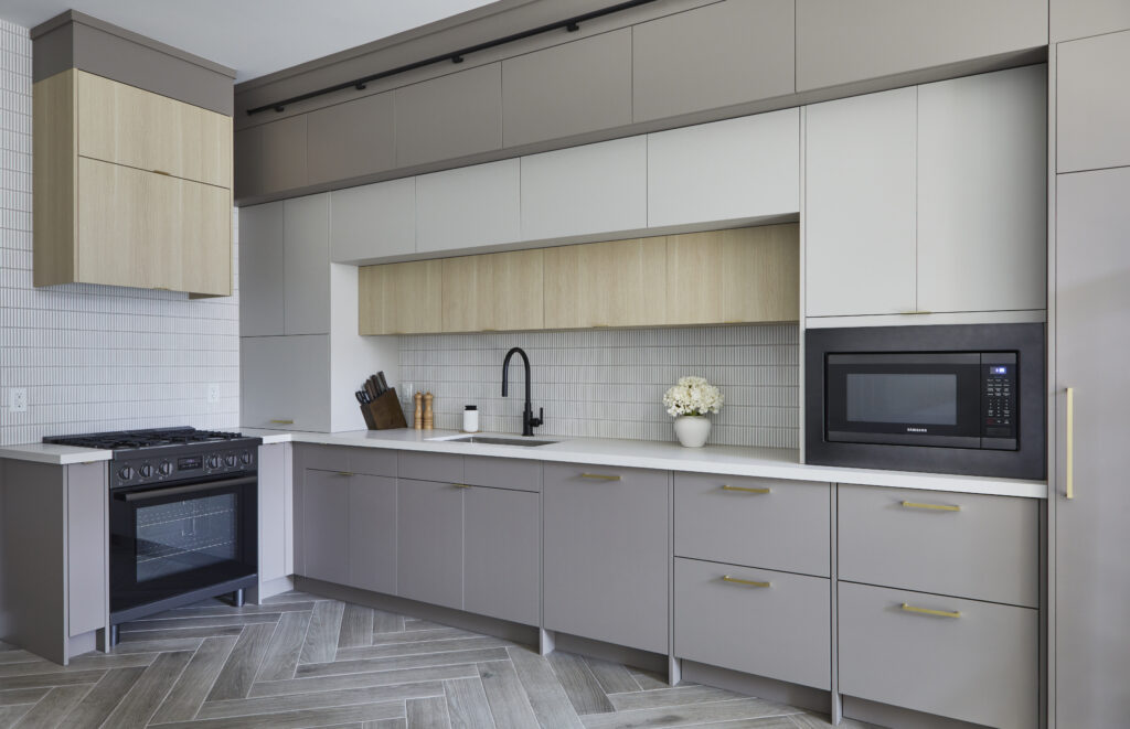 Modern Toronto condo kitchen renovation featuring gray and beige cabinets, white countertops, black stove, built-in microwave, black faucet sink, knife block, utensil holder, potted flowers, and light herringbone wood flooring.