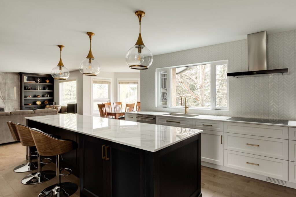 Modern kitchen with a large island featuring a marble countertop, three pendant lights, wooden bar stools, white cabinets, a window, and a view of the dining and living areas in the background.