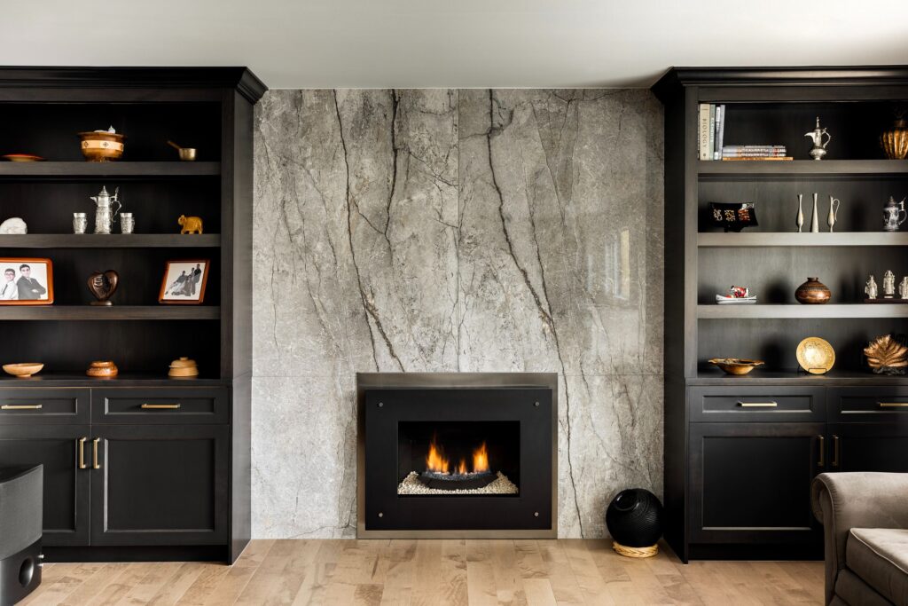 Modern living room with a marble fireplace centered between two black built-in bookshelves displaying decorative items, books, and photos. Light wooden floor contrasts with the dark cabinetry.