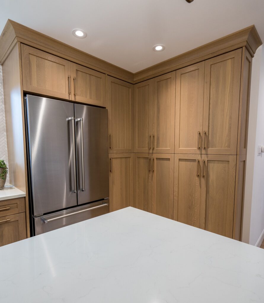 Modern kitchen with light wood cabinets, a stainless steel French door refrigerator, and a white marble island countertop. Recessed lighting brightens the clean, minimalist space.