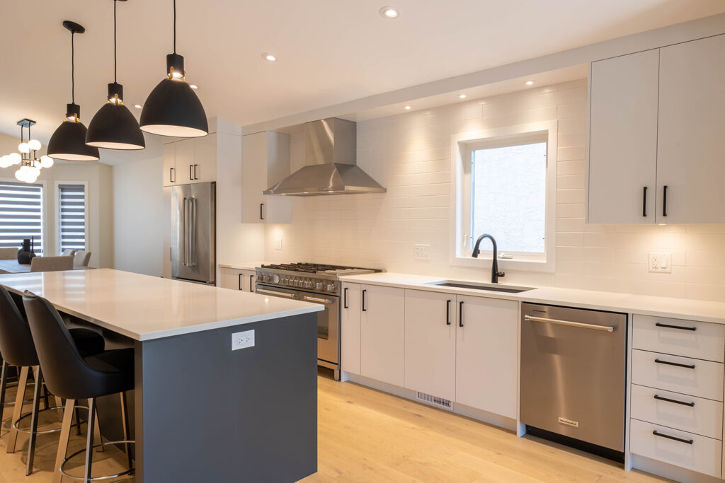Modern kitchen with white cabinets, stainless steel appliances, a central island with black stools, pendant lights above, light wood floor, and a window over the sink.