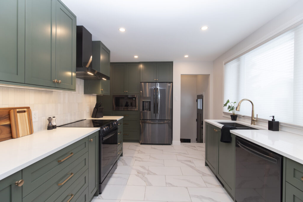 Modern kitchen with green cabinets, white countertops, stainless steel appliances, gold hardware, a farmhouse sink, and large window with blinds; bright, clean, and minimalistic design.