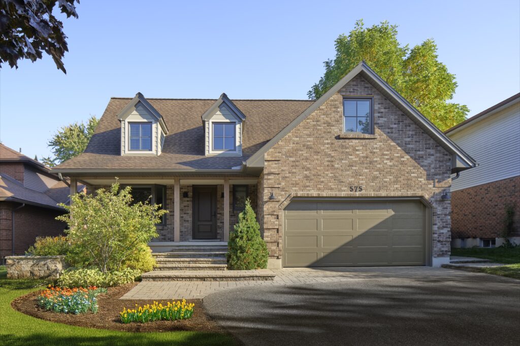 A two-story brick house with a large front porch, steps leading up to the entrance, a double garage, and a well-maintained garden with flowers and shrubs on a sunny day.