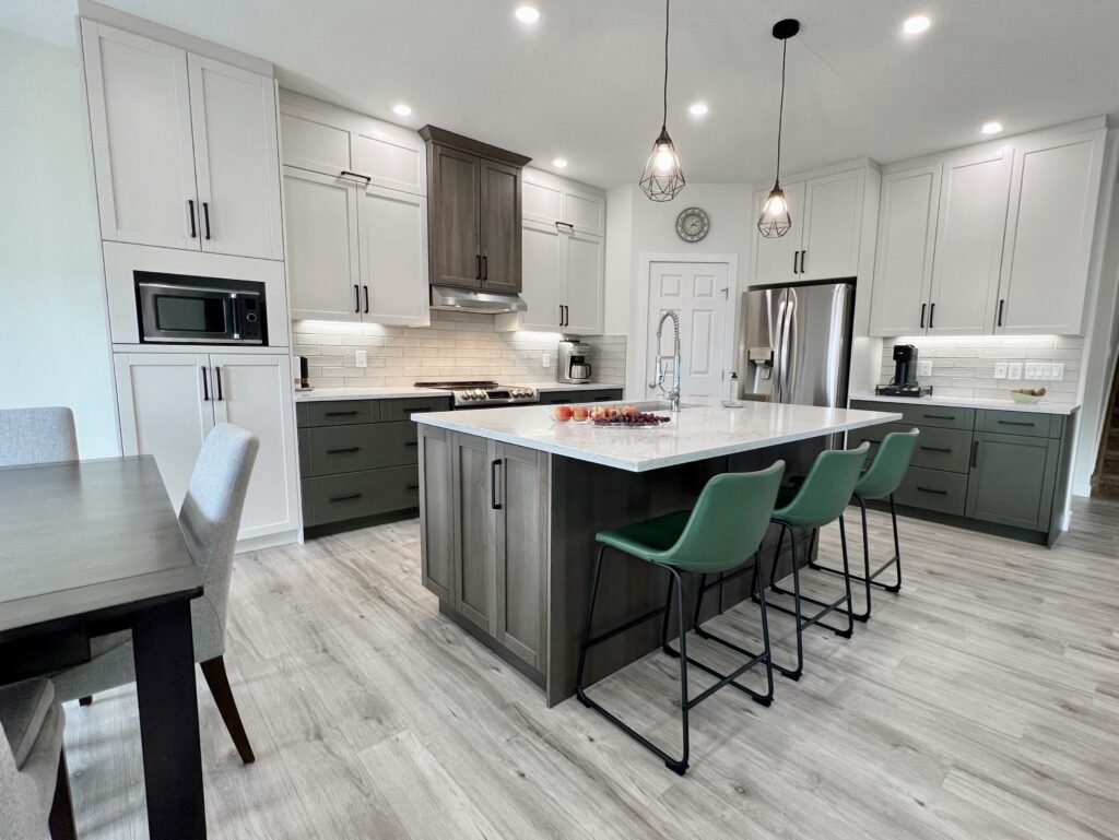 Modern kitchen with white cabinets, a large island with marble countertop, three green barstools, stainless steel appliances, pendant lights, and a dining table with chairs on light wood flooring.