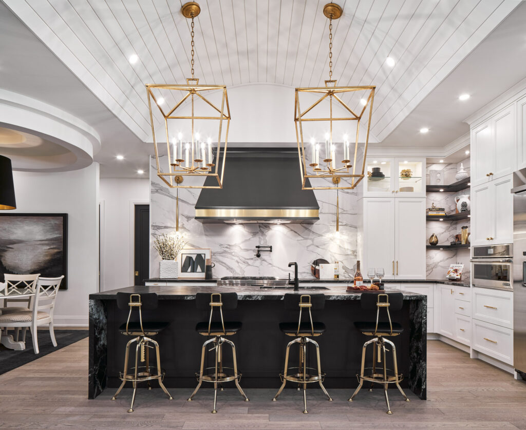 Modern kitchen with black and white decor, gold accents, marble backsplash, island with five black and gold barstools, two large gold pendant lights, and open shelves with decorative items.