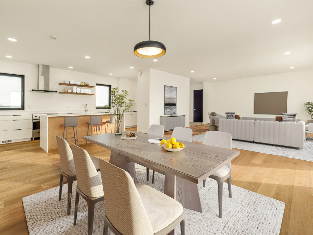 Open-plan living space with a modern kitchen, wooden dining table set for six, barstools at a breakfast island, and a cozy living area with a light sofa and coffee table on wood flooring. Large windows provide natural light.