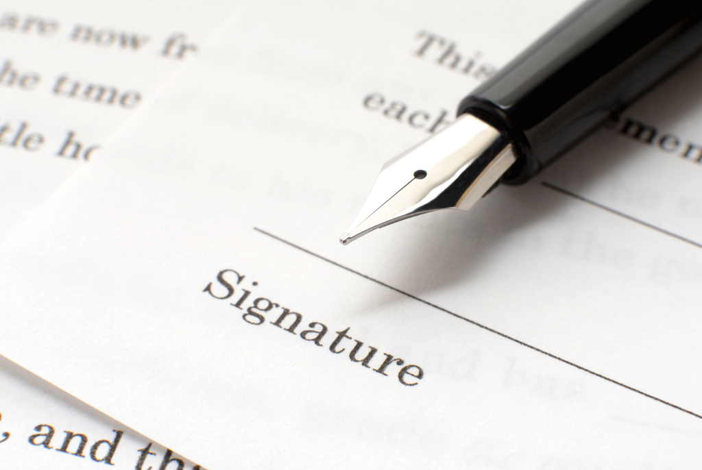 A close-up of a fountain pen resting on a document, with the word Signature printed on a blank line, indicating a place to sign the paper.
