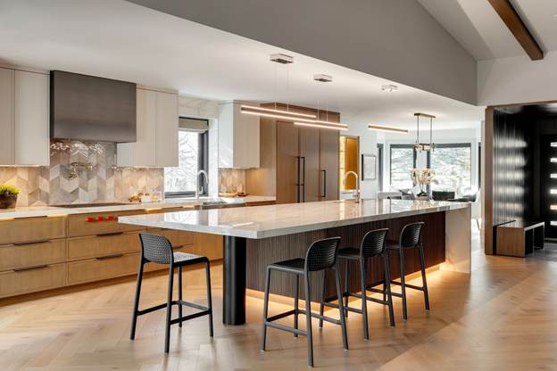 Modern kitchen with a large marble island, four black bar stools, wood cabinetry, geometric tile backsplash, pendant lights, and floor-to-ceiling windows letting in natural light.