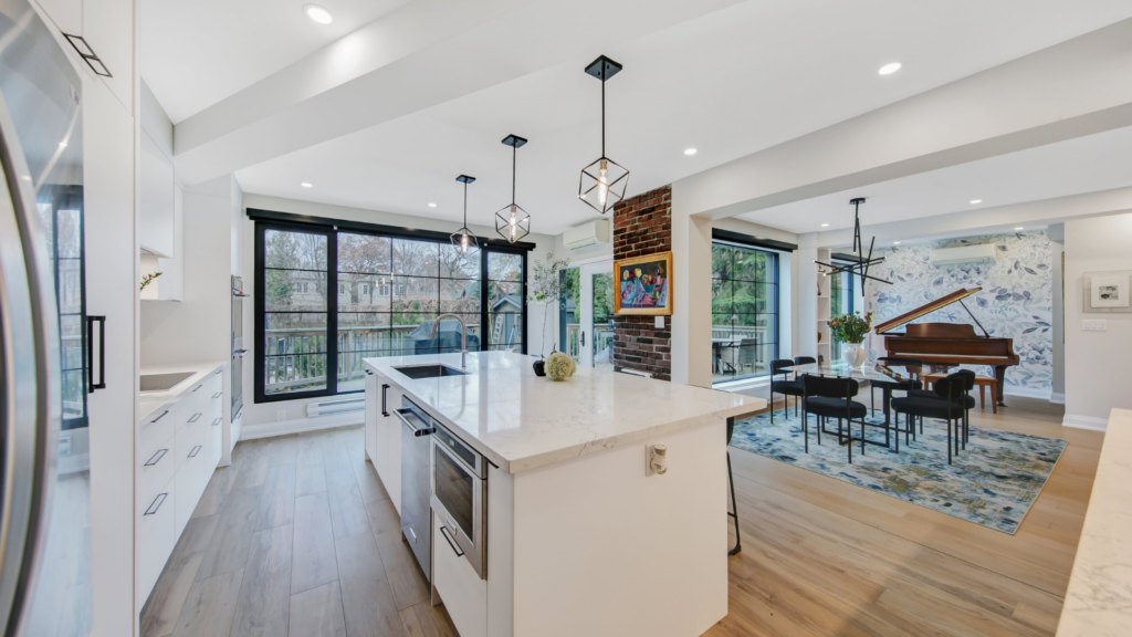 Modern open-concept kitchen and dining area with white cabinets, marble island, large windows, pendant lights, and a grand piano. Bright and stylish interior by RenoMark members—CHBA National Awards 2026 contenders.