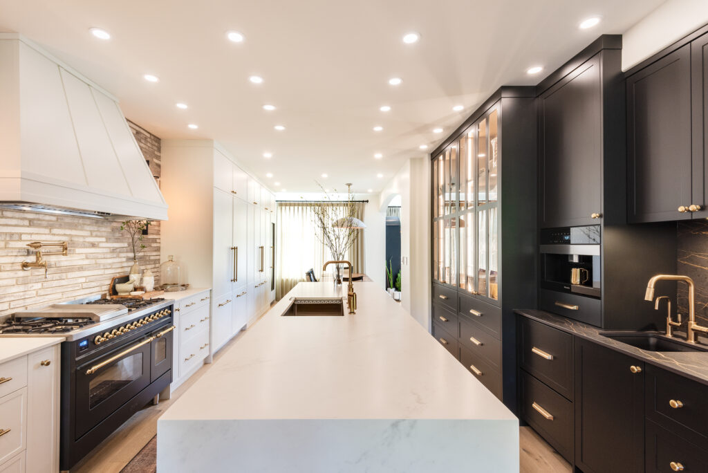 Modern kitchen with white marble island, dark cabinets, built-in appliances, a gas stove, white cabinetry, brick backsplash, under-cabinet lighting, and a vase with branches on the island. Bright and spacious with recessed lighting.