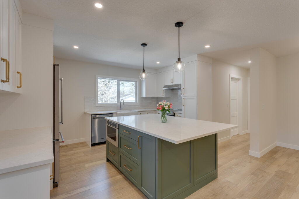 Modern kitchen with white cabinets, a green island, pendant lights, wood flooring, stainless steel appliances, and a vase of flowers on the island. Bright and spacious with natural light from a window over the sink.