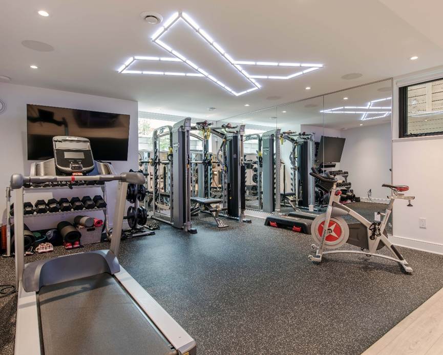 A modern home gym with a treadmill, stationary bike, free weights, and strength training machines, featuring large mirrors, rubber flooring, and unique LED ceiling lights.