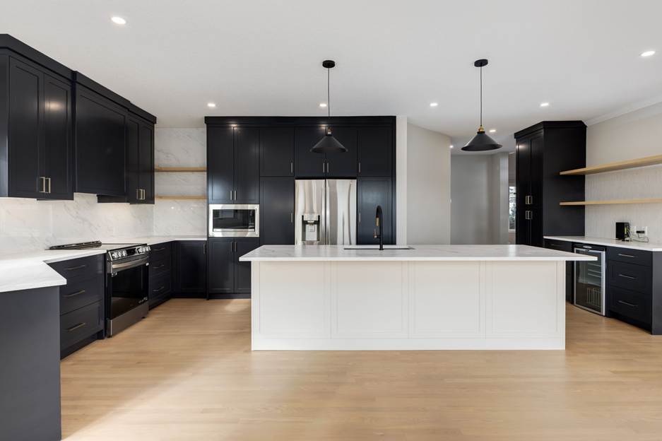 Modern kitchen with black cabinets, white countertops, a large white island, stainless steel appliances, wood flooring, pendant lights, and open shelves along the right wall.