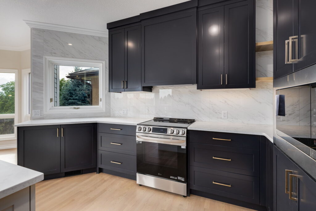 Modern kitchen with dark cabinets, brass handles, white marble countertops and backsplash, stainless steel oven, built-in microwave, wooden floor, and a large window letting in natural light.
