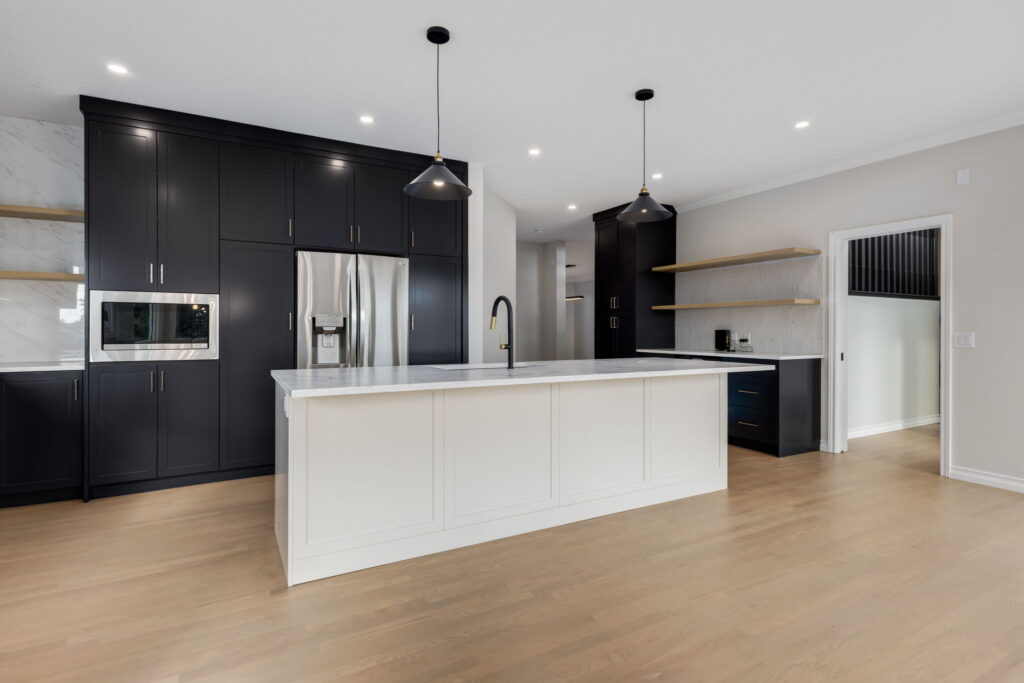 Modern kitchen with black cabinets, stainless steel appliances, a white island with marble countertop, pendant lights, open wood shelves, and light wood flooring.