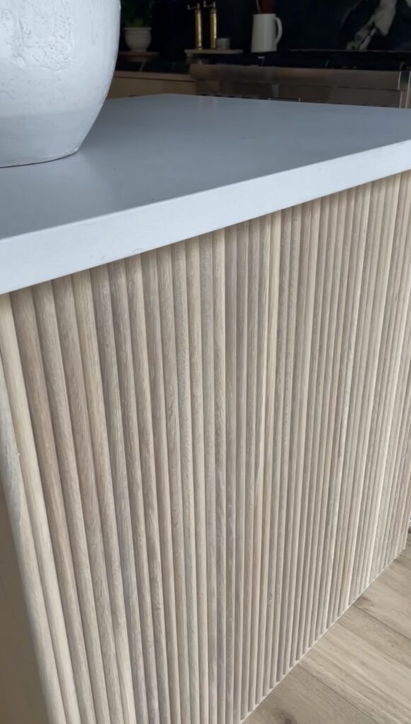 A close-up of a modern cabinet featuring vertical light wood slats beneath a smooth white countertop.