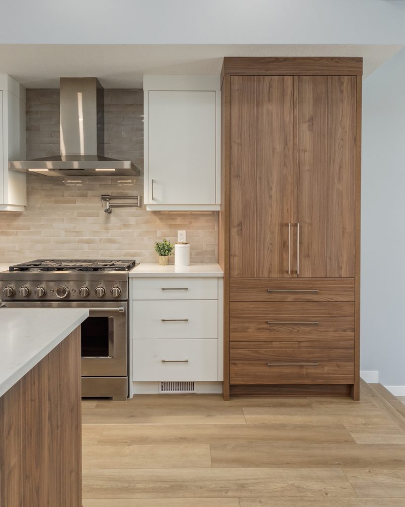 Modern kitchen with wood cabinets, stainless steel stove and hood, white drawers, light beige backsplash, and potted plant on the counter. Light wood flooring complements the contemporary design.