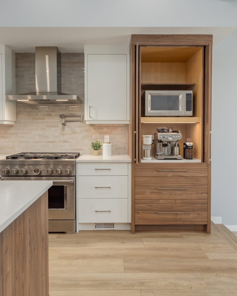 Modern kitchen with stainless steel stove, white cabinets, and a wood cabinet featuring a microwave, coffee maker, and espresso machine on wooden shelves, all set on light wood flooring.