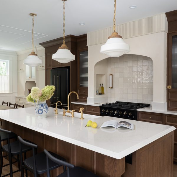 A modern kitchen features a large island with a white countertop, black chairs, pendant lights, wood cabinets, a black stove, and a vase with hydrangeas. Lemons and an open book rest on the island.
