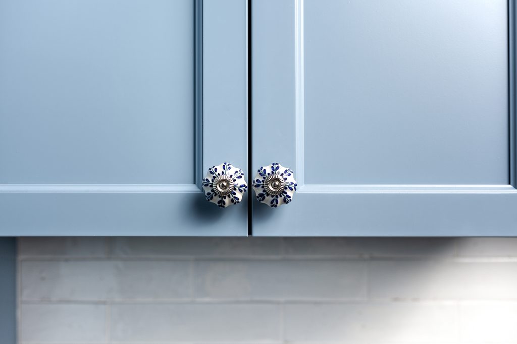 Close-up of light blue cabinet doors with decorative round ceramic knobs featuring a blue and white floral pattern, above a light blue tiled backsplash.