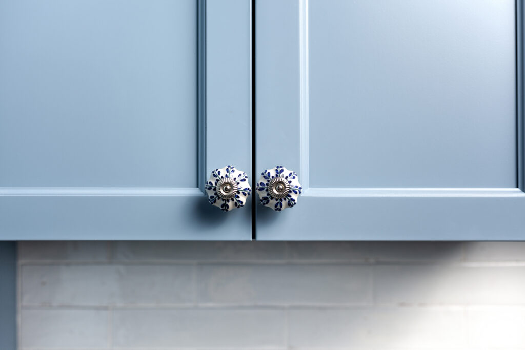 Close-up of two light blue cabinet doors with decorative round knobs featuring blue floral patterns, set above a pale blue tiled backsplash.