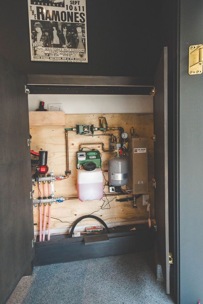 A utility closet with pipes, a water tank, control panels, and a chemical container. A Ramones concert poster is visible above the open closet doors.