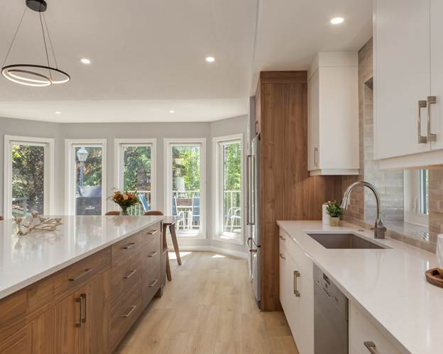 Modern kitchen with wood cabinets, white countertops, stainless steel appliances, island with seating, and large windows letting in natural light.