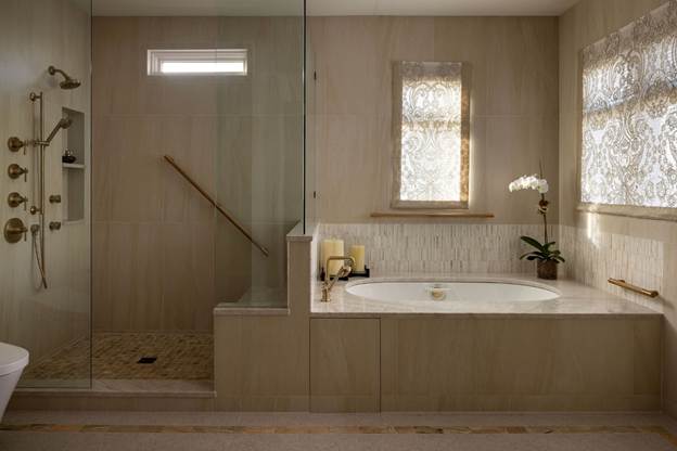 Elegant bathroom with a glass shower, built-in bathtub, candles, and an orchid. Light pours through windows with patterned curtains, creating a calm and inviting atmosphere.