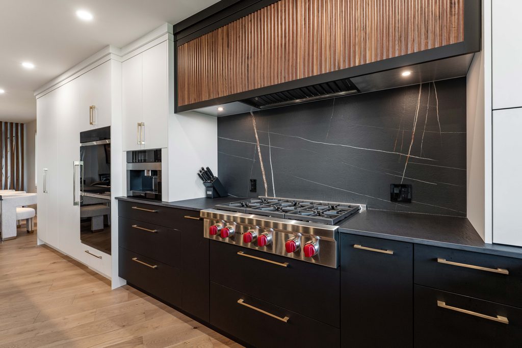 Modern kitchen with black and white cabinets, a stainless steel gas stove with red knobs, black countertop, wood accents, and a black marble backsplash with white and gold veining.